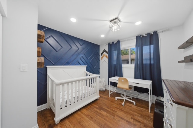 Bedroom with navy accent wall, white crib and desk — angle 2